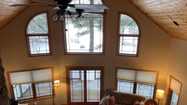 A spacious loft bedroom with a large arched window, a ceiling fan, and a cozy seating area with a couch and lamps. - Lake cabin on Holcombe flowage. Loft views, fire pit, and nearby hiking. (Holcombe)