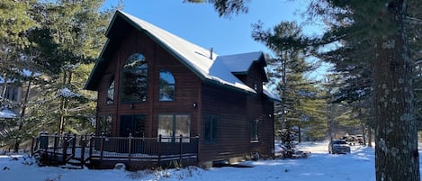 A wooden cabin with a steep roof, large windows, and a porch.