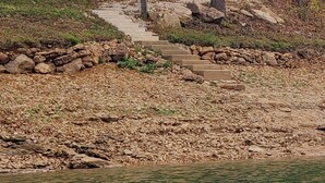 Una cabaña con terraza de madera y una escalera de piedra que lleva a ella, rodeada de árboles y un cuerpo de agua.