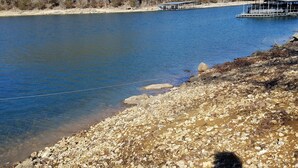 Una costa rocosa con un muelle que se adentra en un lago tranquilo, rodeado de árboles.