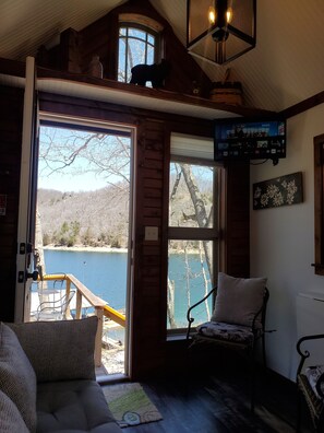 Ein gemütliches Cabin-Interieur mit einem großen Fenster mit Seeblick, einer komfortablen Sitzecke und einem an der Wand montierten Fernseher.
