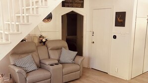 Una sala de estar con un sofá color beige, un tapete estampado, una mesa de centro blanca y una escalera con un letrero que dice "Mege Cottage Islanders Welcome Est. 2021".