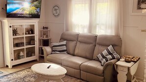 Una sala de estar con un sofá color beige, una mesa de centro blanca, un televisor en la pared y un mueble decorativo.