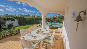 An outdoor patio with a dining table and chairs, a pool in the background, and a bell on the wall. - Casa dos Sonhos Praia da Luz (Luz)