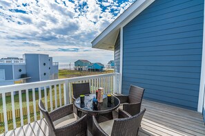 Ein Balkon mit Korbmöbeln und einem Tisch, mit Blick auf einen Strand und weitere Gebäude.