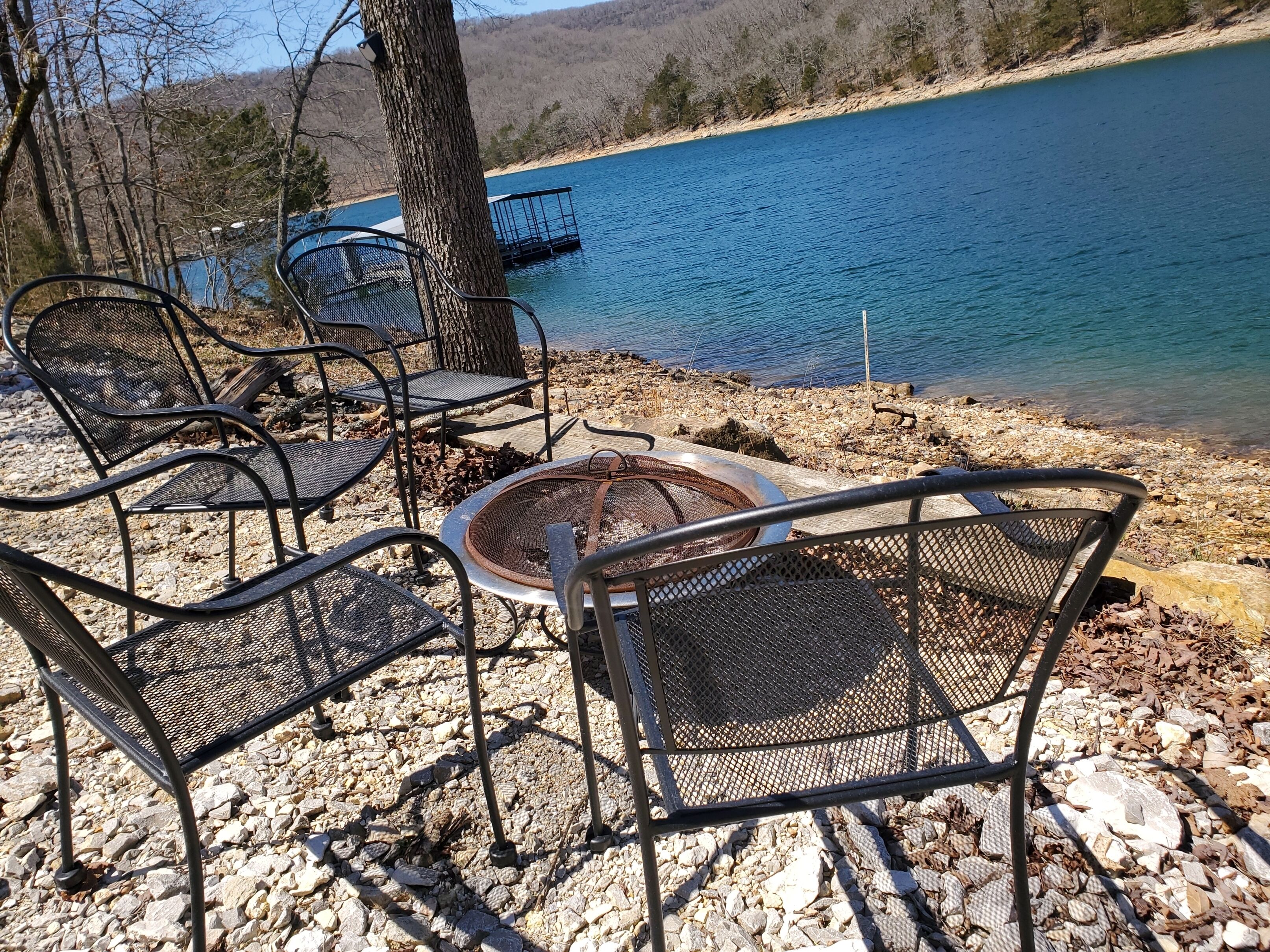 A lakeside seating area with metal chairs and a fire pit.