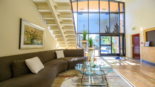 A modern lobby with a curved staircase, a reception desk, and a large window offering a view of the outdoors. - Studios Inn (San Jose)