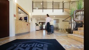 A hotel lobby with a reception desk, a staircase, and a black carpet with "studios inn" text. - Studios Inn (San Jose)