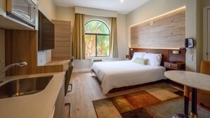 A hotel room with a bed, a small table, a sink, and a microwave. - Studios Inn (San Jose)