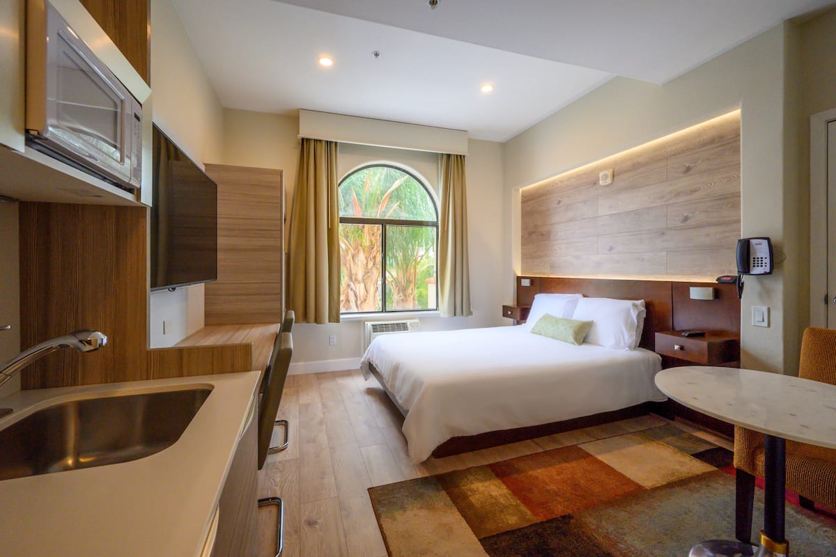 A hotel room with a bed, a small table, a sink, and a microwave.