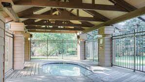 A covered outdoor swimming pool with a wooden ceiling structure, surrounded by a metal fence and a paved deck. - Cute kid-friendly condo next to Dollar Mountain (Sun Valley)