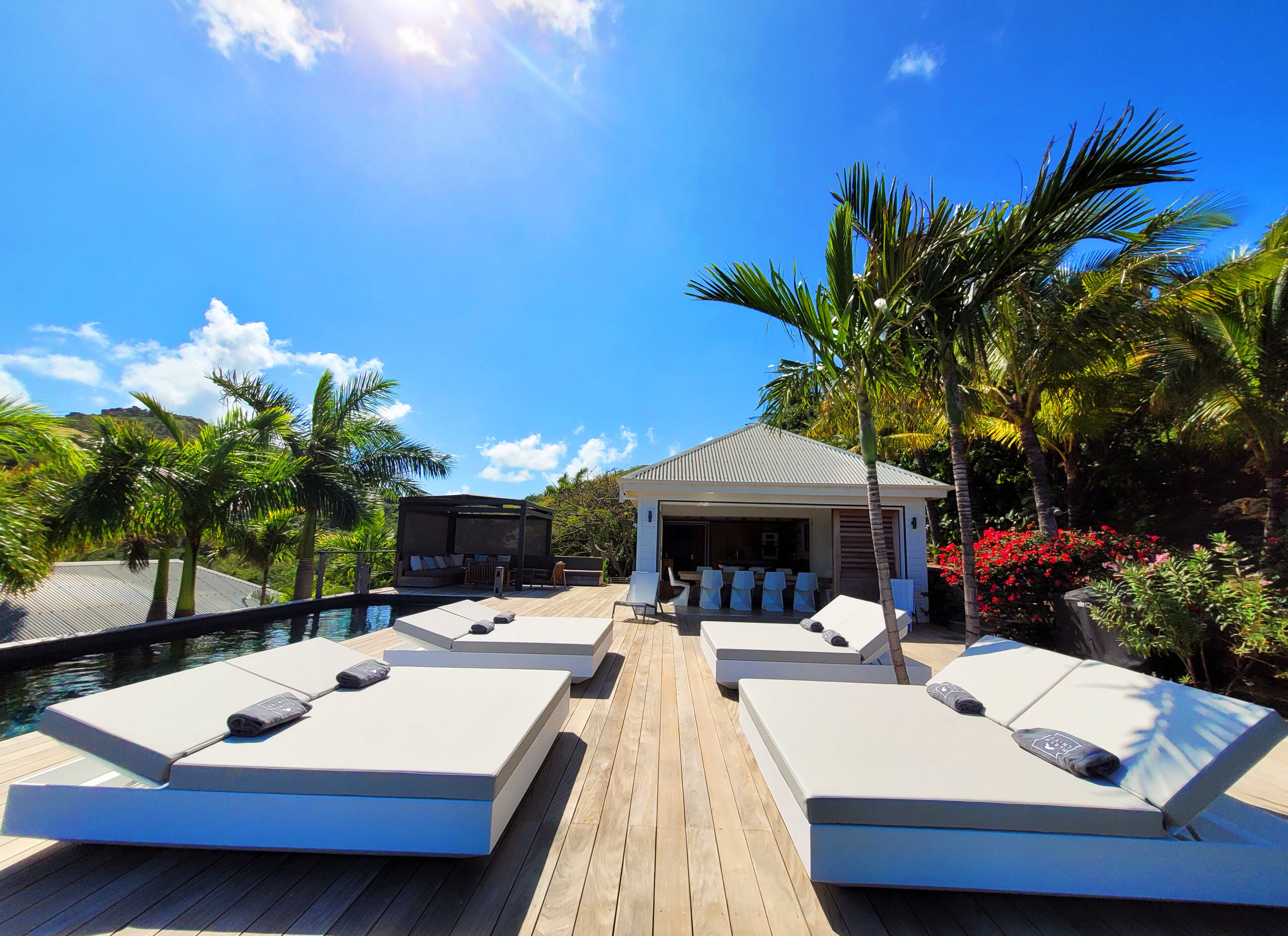 Zona de piscina con sillones de descanso, un espacio de estar techado y vista a la piscina.
