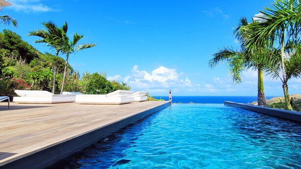 A pool with a wooden deck and palm trees, overlooking a clear blue sky and ocean. - Villa Coco Rock | Ocean View - Located in  Beautiful Petit Cul de Sac with Private Pool (Saint Barthélemy)