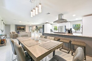 Cozinha moderna com ilha central, eletrodomésticos de aço inoxidável e área de jantar com mesa e cadeiras de madeira.