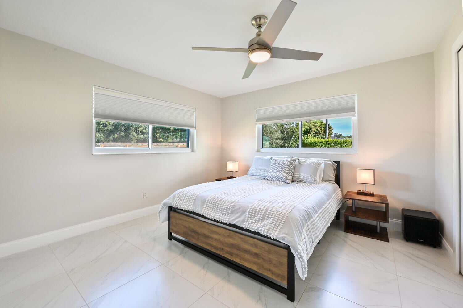 A bedroom with a bed, two bedside tables, a ceiling fan, and two windows with blinds.