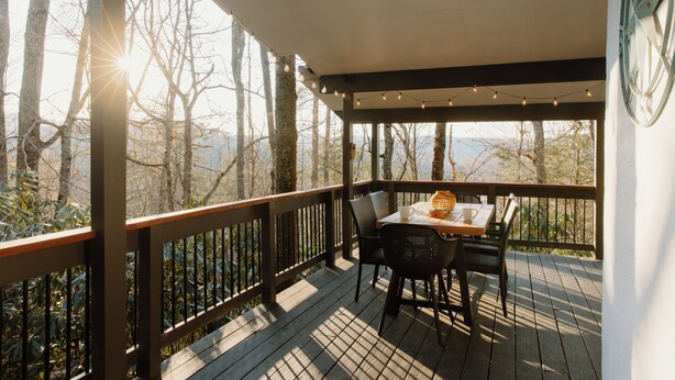 Um deck de madeira com uma mesa e cadeiras, com vista para uma área arborizada.