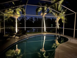 A pool area with a glass enclosure, lounge chairs, and palm trees. - Designer Lakefront Haven ‘ (Naples)