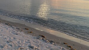 Ein Strand mit ruhigem Wasser, das den Himmel spiegelt, einem sandigen Ufer und einem fernen Horizont.