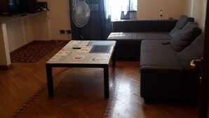 A living room with a sofa, a coffee table, a TV, and a fan. - Modern and cosy apartment in Genoa, Italy (Genova)