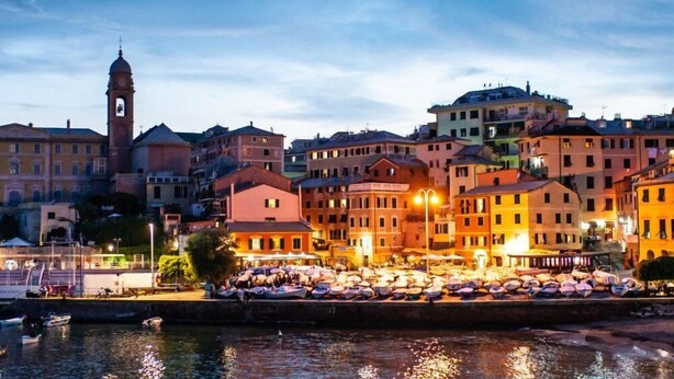 A waterfront town with historic buildings, a prominent clock tower, and boats lined up along the quay. - Modern and cosy apartment in Genoa, Italy (Genova)
