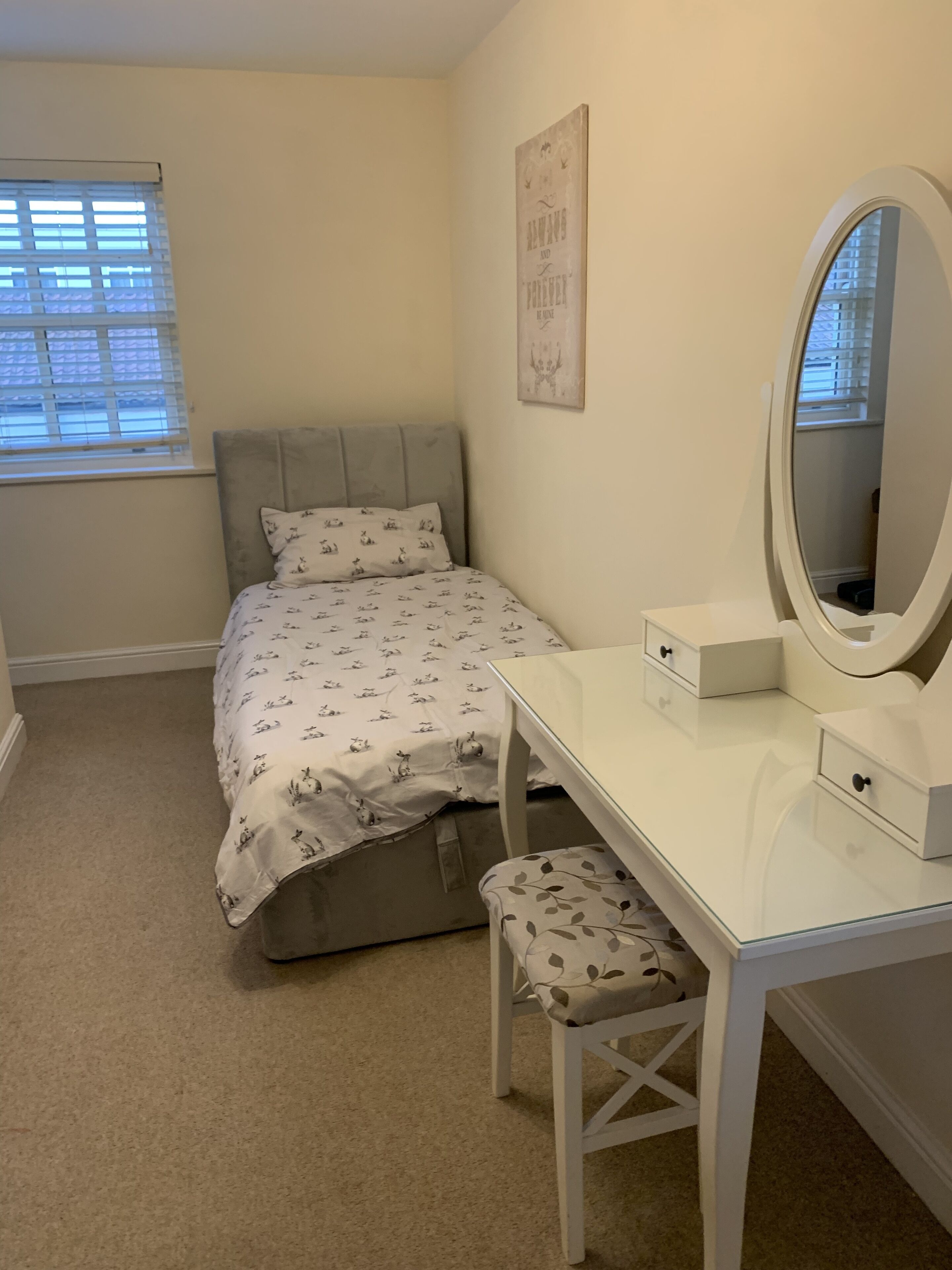 A bedroom with a bed, a bedside table, a chair, a dresser, a mirror, and a window with blinds.