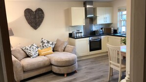 A modern kitchen with white cabinets, a stainless steel range hood, and a black countertop. There is a beige sofa with patterned cushions and a heart-shaped wall decoration. - 2-Bed Duplex Sleeps 3 with Fireplace (doncaster)