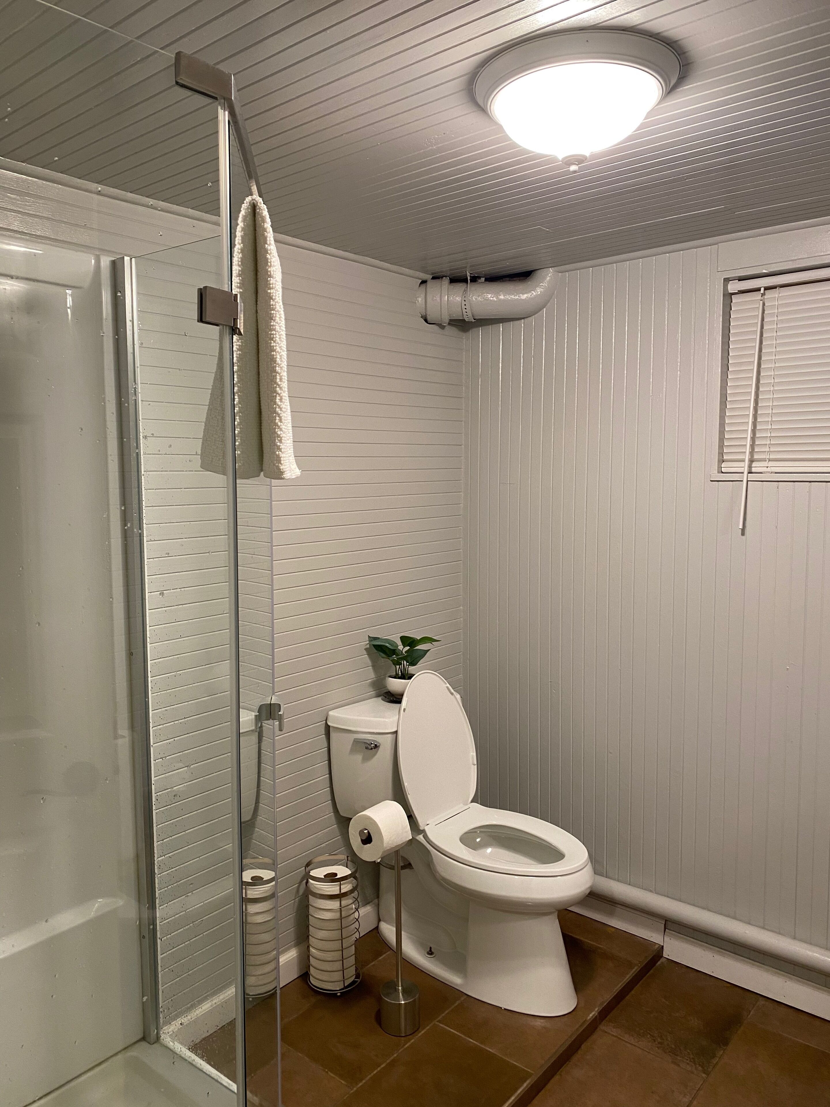 Une salle de bain équipée de toilettes, d’une douche et d’une fenêtre avec des stores.