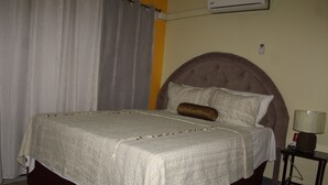 A neatly made bed with a headboard, a bedside lamp, and a curtain.