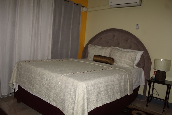 A neatly made bed with a headboard, a bedside lamp, and a curtain.