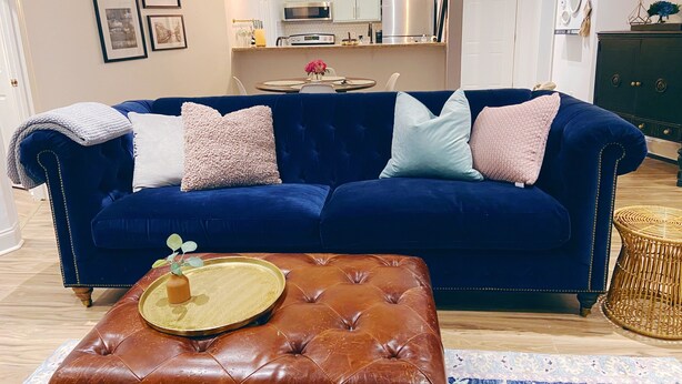 A living room with a dark blue sofa, a brown leather ottoman, and a round coffee table with a tray.