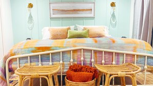 A bedroom with a bed, two wicker chairs, a wicker basket, and a painting on the wall.