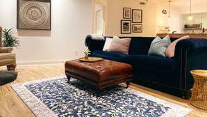 A living room with a dark blue sofa, a brown leather ottoman, and a patterned rug.