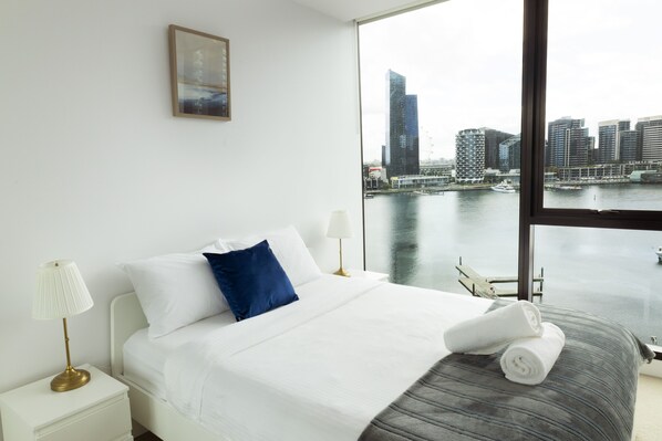 A hotel room with a large window offering a view of a city skyline and water body.