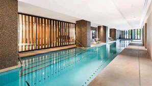En lång inomhuspool med klart vatten, ett kaklat golv och en modern design med en glasvägg och träribbor på ena sidan.