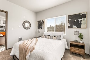 A bedroom with a large bed, a bedside table, a lamp, and a window with blinds.