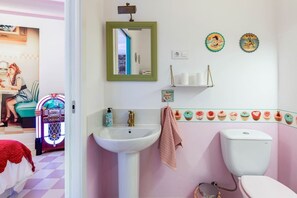 Ein Badezimmer mit einem weißen Waschbecken, einem spiegel mit grünem Rahmen, einer Toilette und einem Regal mit Pflegeartikeln.