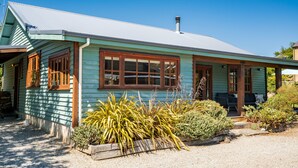 A single-story house with a gabled roof, wooden windows, and a front porch. - The Cottage on the Hill - Wānaka Holiday Home (Wanaka)