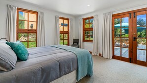 A bedroom with a bed, a desk, and a view of the outdoors through large windows. - The Cottage on the Hill - Wānaka Holiday Home (Wanaka)