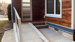 A modern building with a wooden exterior, a glass door, and a concrete ramp leading to the entrance.