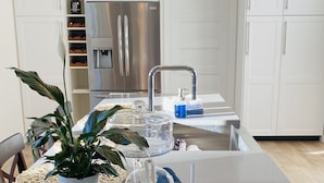 A modern kitchen with white cabinetry, a stainless steel refrigerator, a built-in oven, and a large island with a sink.