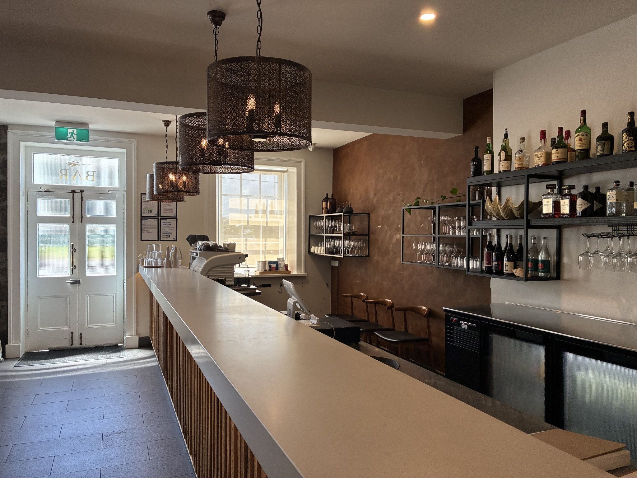 A bar area with a long counter, multiple hanging lights, and a wine and liquor display.