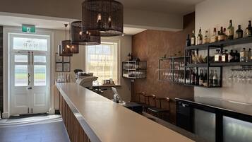 A bar area with a long counter, multiple hanging lights, and a wine and liquor display.