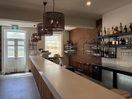 Zona de bar con una barra larga, varias luces colgantes y una exhibición de vinos y licores.