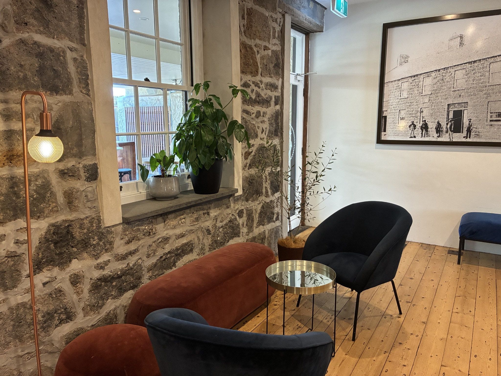 A room with a stone wall, a window, a potted plant, a blue chair, a red chair, and a table.