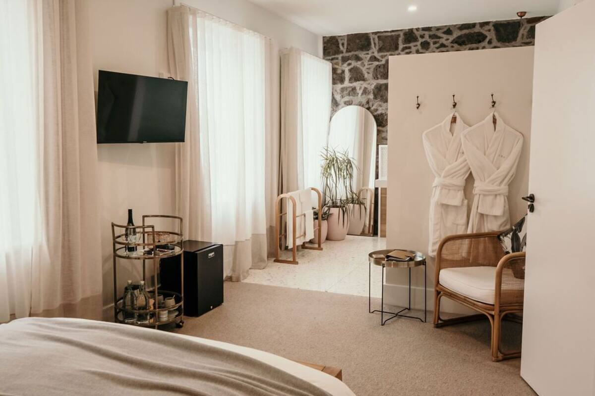 A hotel room with a bed, a TV, a mirror, a chair, and a wardrobe with robes.