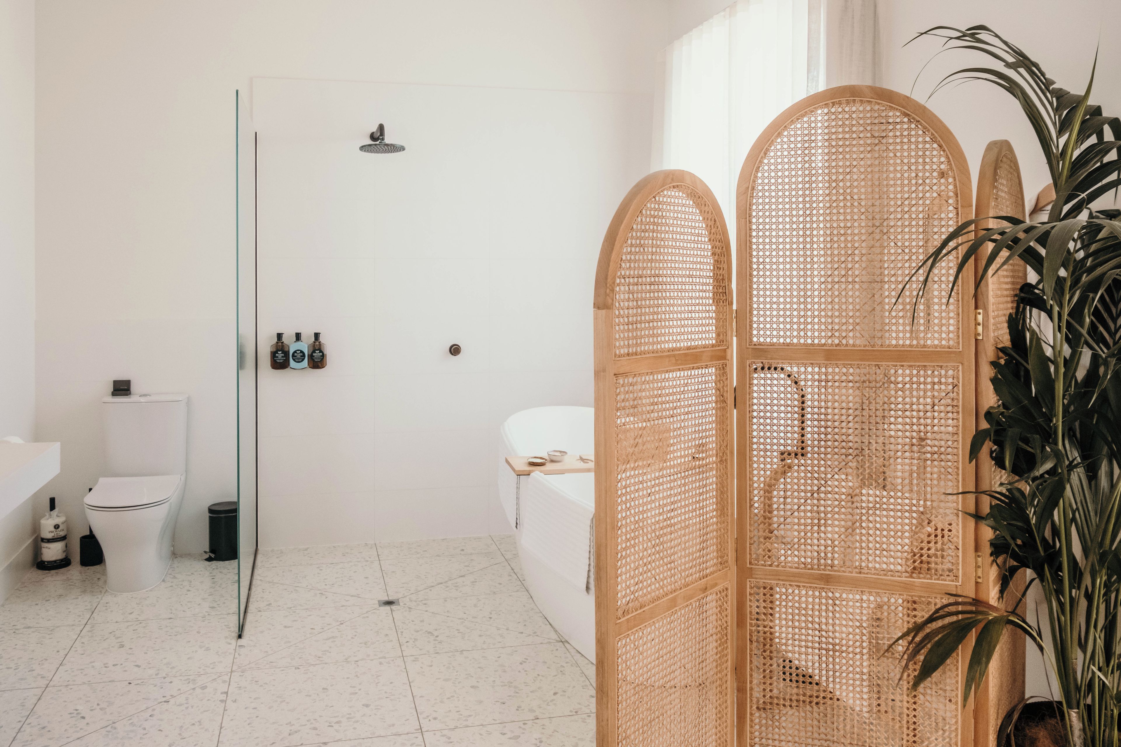 Baño con inodoro, bidé y zona de ducha. Cuenta con una mampara de vidrio y un separador decorativo de madera.