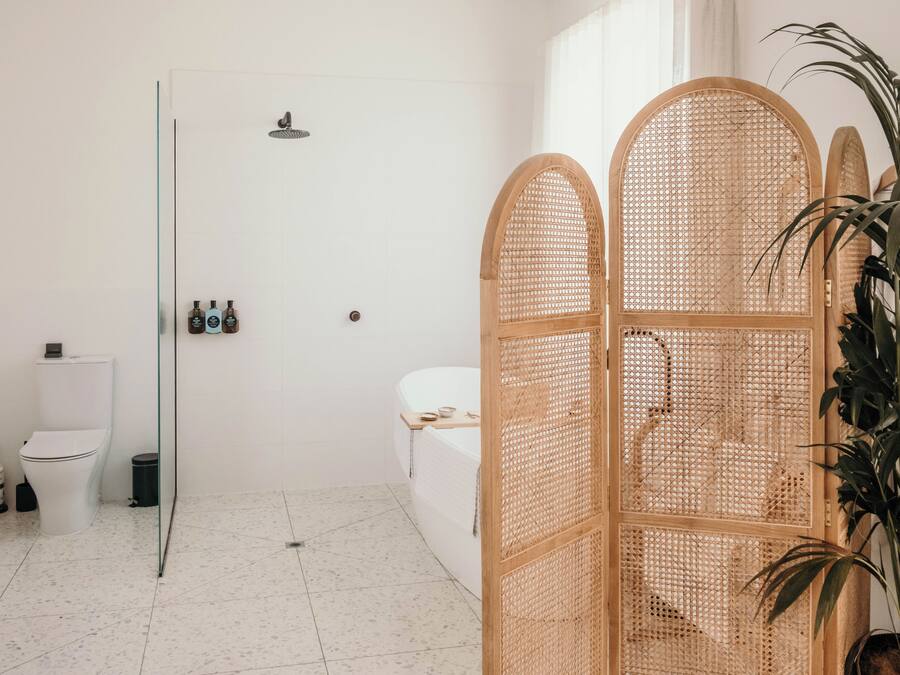 Baño con inodoro, bidé y zona de ducha. Cuenta con una mampara de vidrio y un separador decorativo de madera.