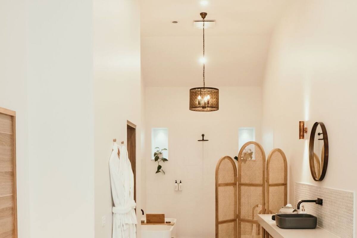 A hotel room with a bed, a desk with a sink, a mirror, and a shower area.
