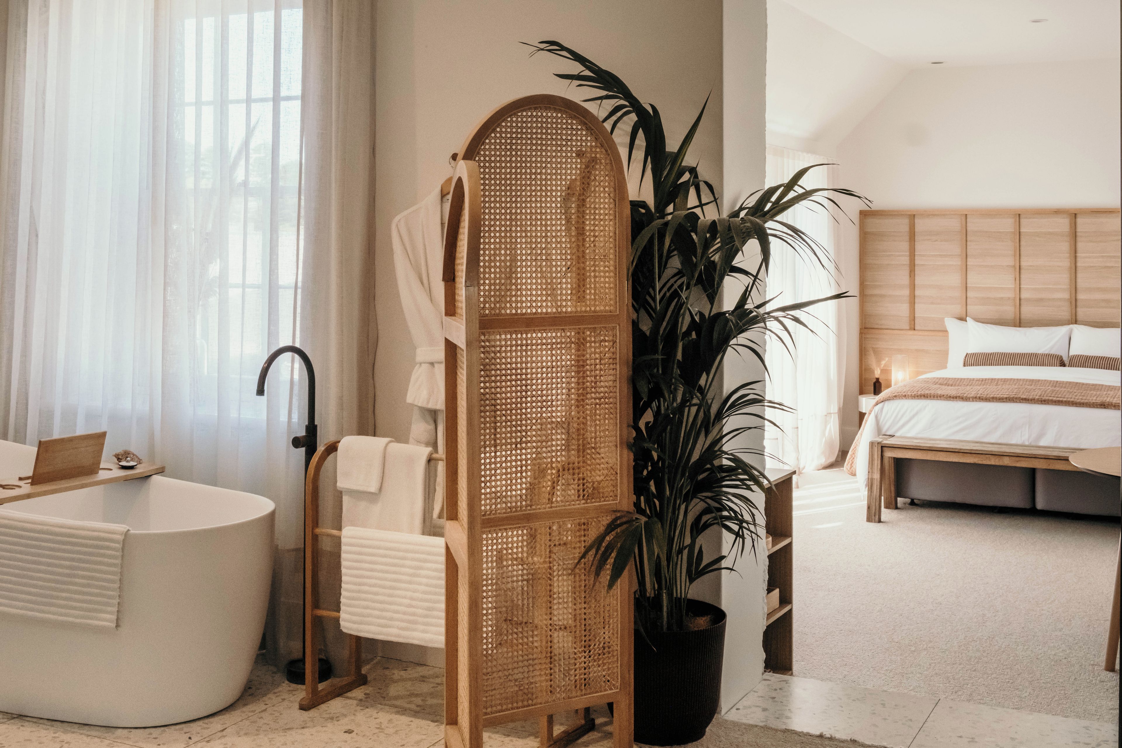 A modern bathroom with a freestanding bathtub, a large potted plant, and a wooden rack.