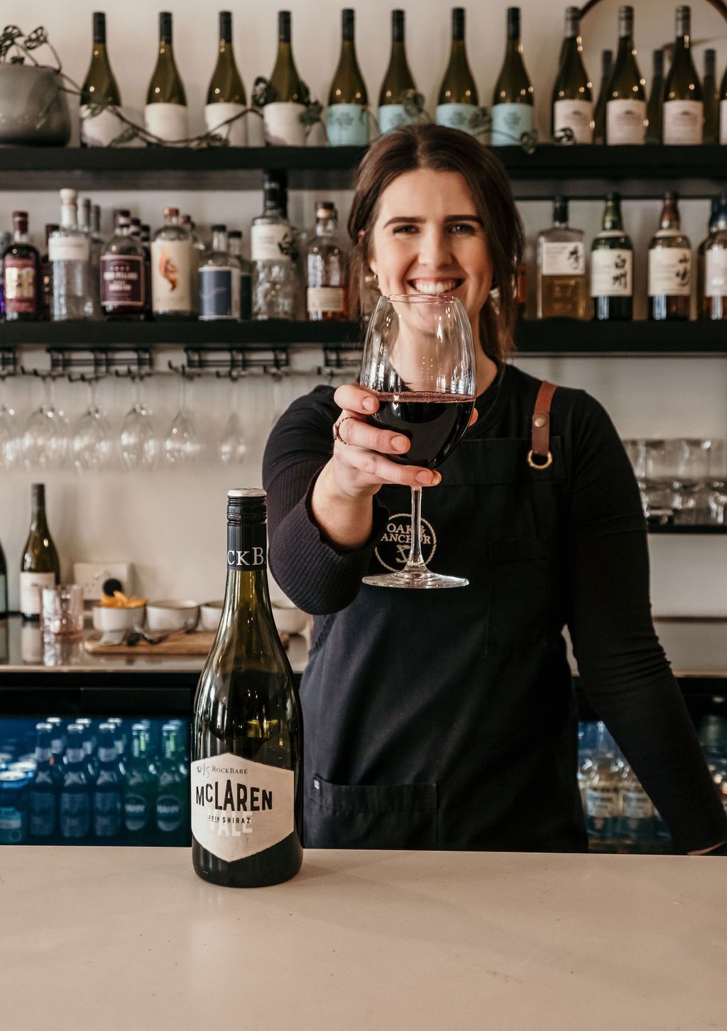 A person holding a wine glass with a bottle of McLaren wine in front of them.